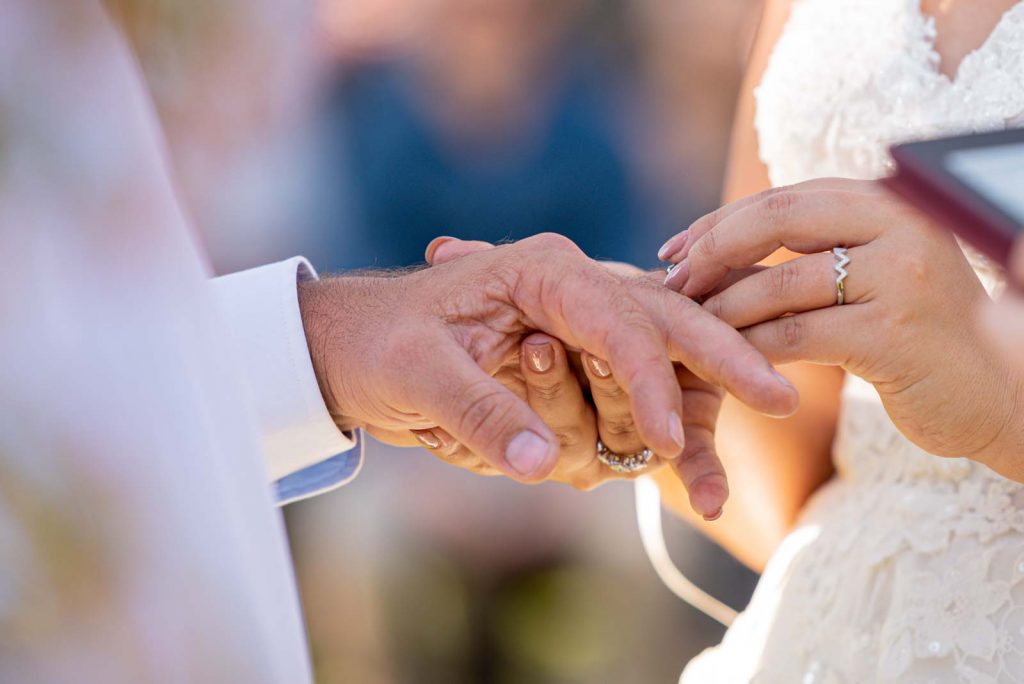 Bride slips ring onto Groom finger, close up.