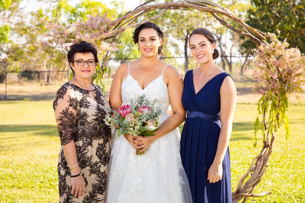 Bride poses at wedding arch with family.