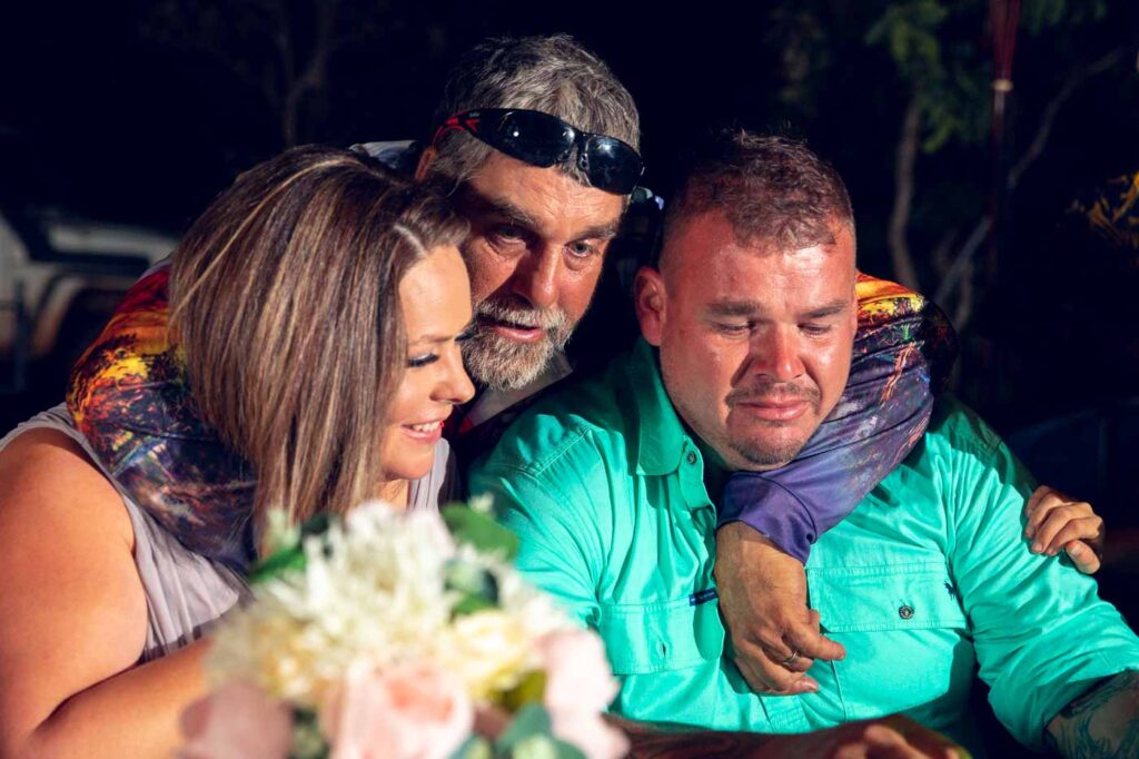 Father hugs wedding couple at rural wedding. Lake Bennet NT. Groom has tears.