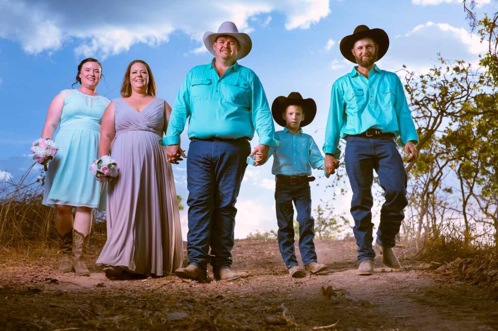 Bridal party in country dress walk towards camera along dusty track.